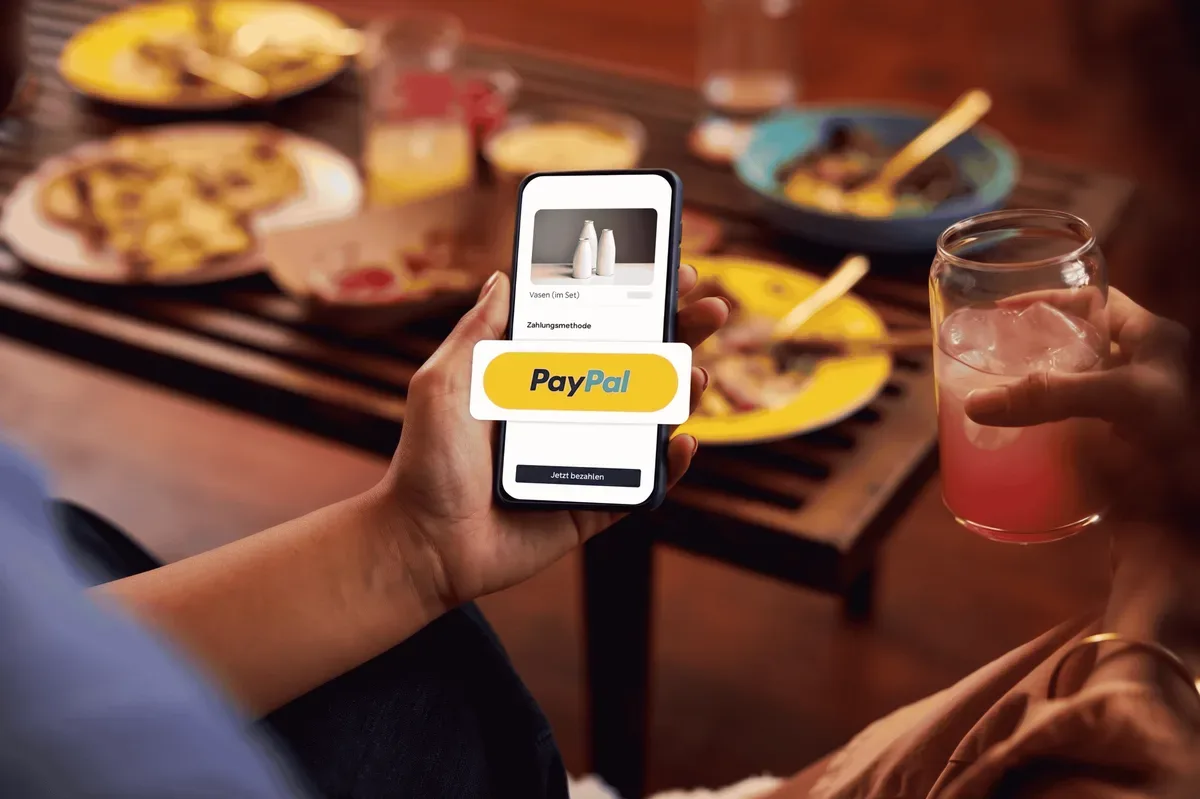 Gedeckter Tisch mit Essen, im Vordergrund ein Smartphone mit geöffnetem PayPal-Bezahlvorgang